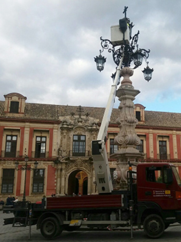 Trabajos de mantenimiento en una farola histórica frente a un edificio barroco en una plaza urbana.