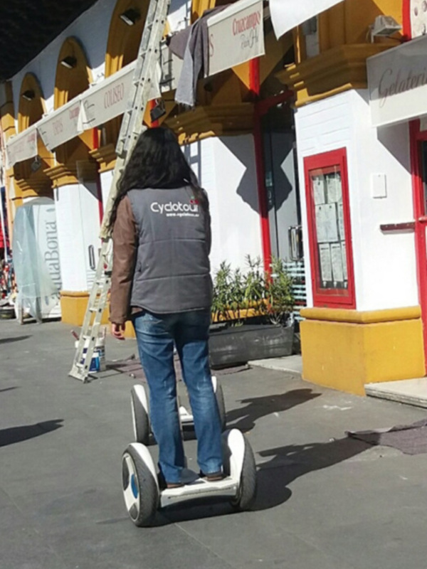 Persona montada en una scooter eléctrica en una calle con edificios históricos y comercios locales.