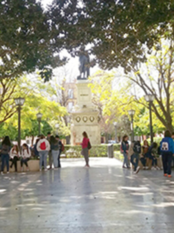 Patio con estatua y personas caminando en un campus universitario.