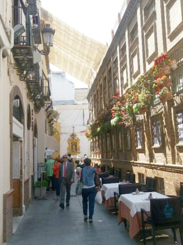 Calle adoquinada con mesas de terraza en un edificio de estilo colonial, decorado con flores y cuadros.