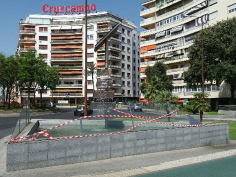 Fountain with red and white tape indicating restricted access in a city square surrounded by apartment buildings.