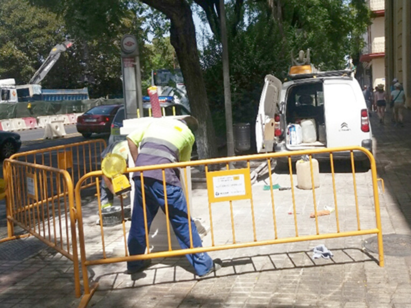 Trabajador de construcción trabajando en una obra en la calle, con una camioneta y una grúa en el fondo.
