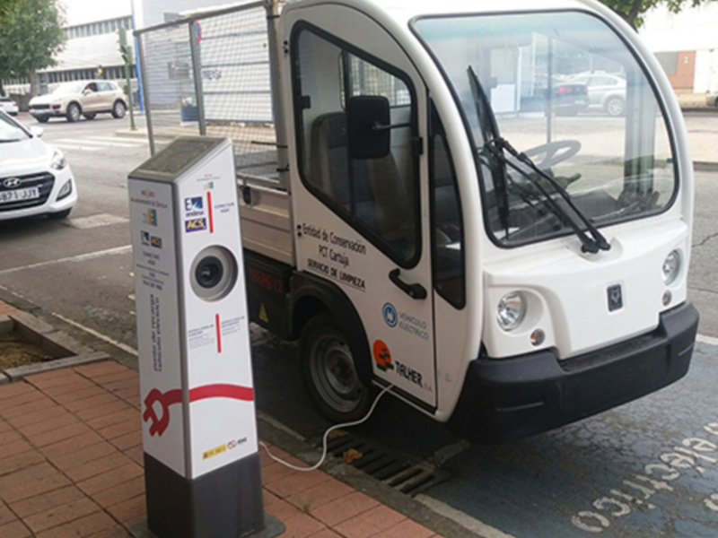 Vehículo eléctrico de la empresa E-Taller, estacionado en un aparcamiento público con un cargador de electricidad.