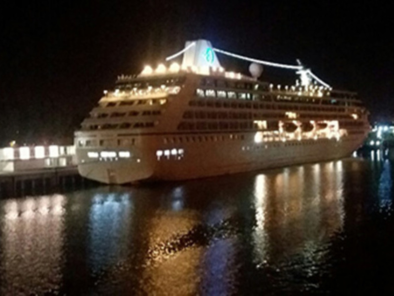 Barco de crucero en el puerto nocturno, iluminado con luces blancas y azules, reflejándose en el agua ligeramente helada.