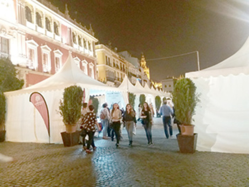 Feria nocturna en plaza histórica con puestos bajo tiendas blancas y gente caminando.