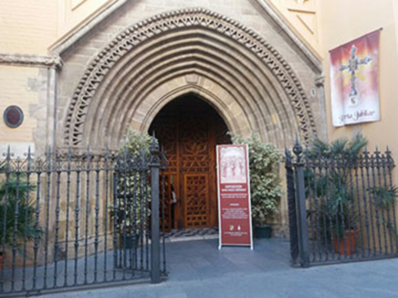 Entrada principal de una iglesia con una puerta de madera tallada y un letrero informativo en el lado derecho.