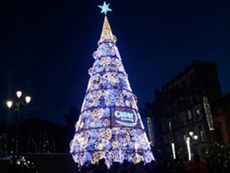 Árbol de Navidad iluminado con luces azules y estrellas en la cima, en un entorno urbano con edificios y farolas.