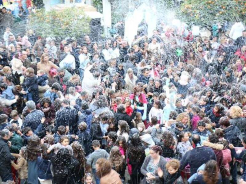 Una multitud de personas reunidas en un evento al aire libre, con una fuente de agua en el centro. La gente está vestida informalmente y parece estar disfrutando del evento.