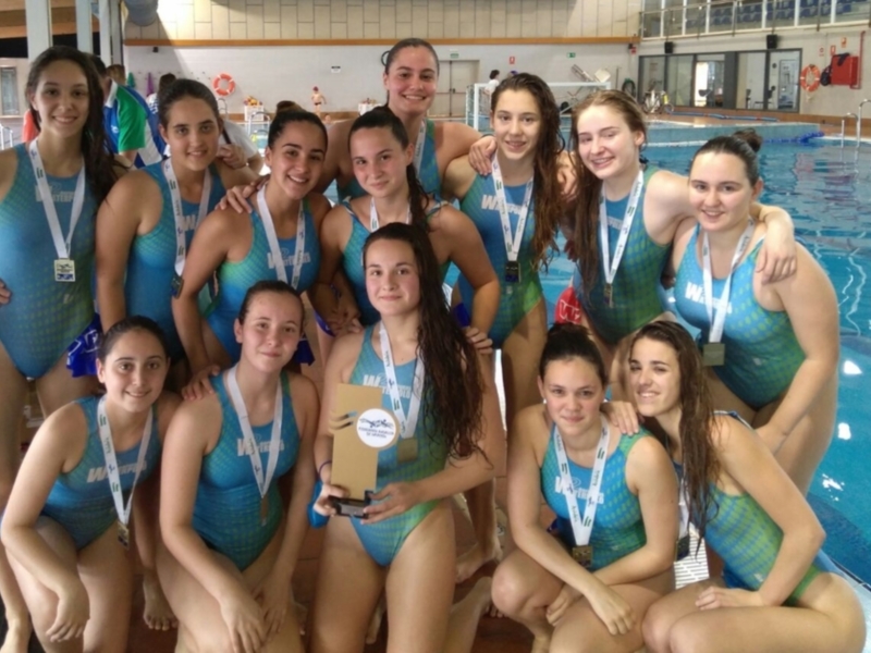 Equipo de natación femenina posando con medallas en una piscina.