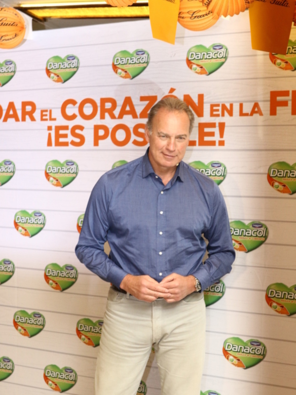 Un hombre posa frente a un fondo con el logo de Danacol, con un diseño de corazones en forma de corazón y el texto '¡ES POSIBLE!' en el centro.