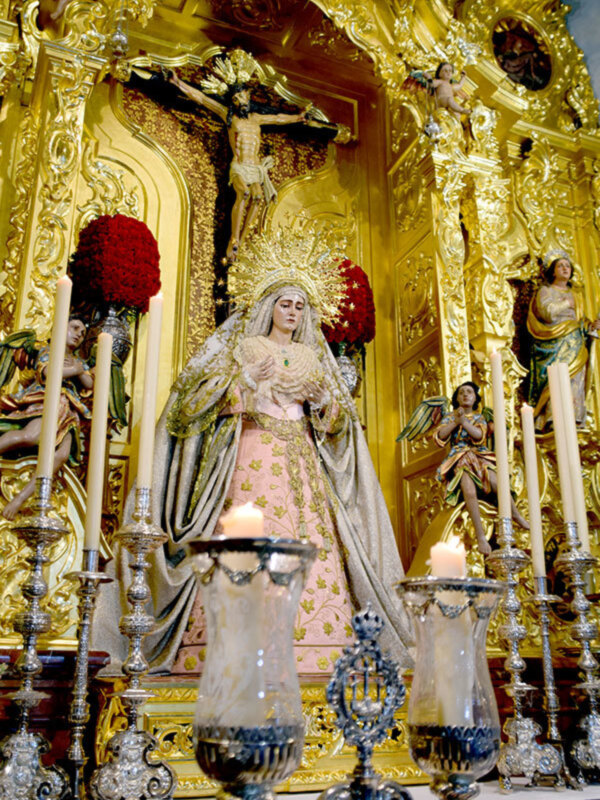 Altar con estatua de la Virgen María y Crucificado en un interior ornamental y dorado.