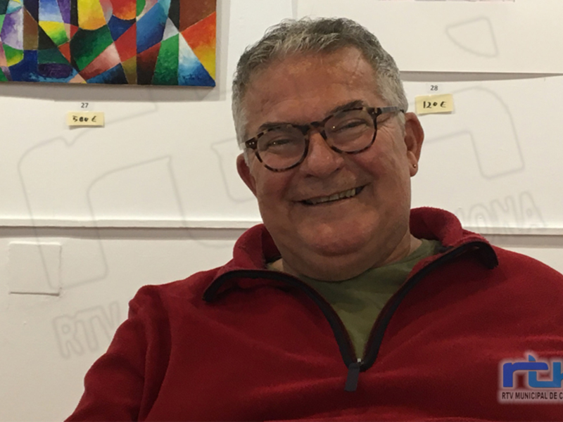 Un hombre sonriente frente a una pared con carteles de precios de arte.