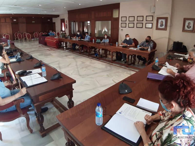 Reunión de trabajo en una sala de conferencias con participantes sentados alrededor de una larga mesa, utilizando máscaras y documentación.