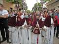 Niños vestidos con trajes de ceremonia tradicionales, posiblemente para una celebración religiosa o festiva. Ellos llevan máscaras faciales y están en una calle con edificios y árboles al fondo.