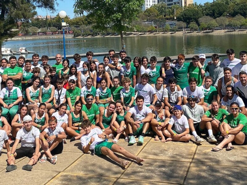 Grupo de jóvenes en un evento deportivo junto a un lago, posando para la foto.