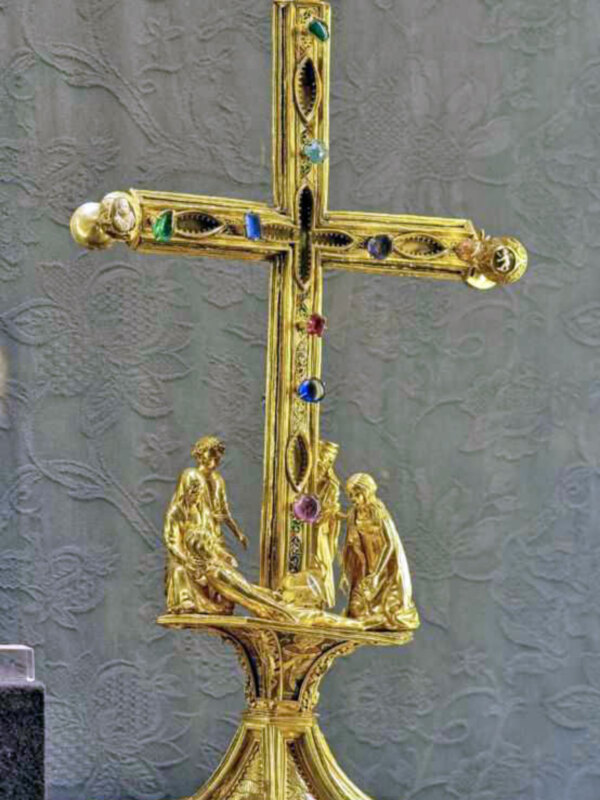 Cruz dorada ornamentada con piedras preciosas y figuras de ángeles, símbolo religioso elaborado.