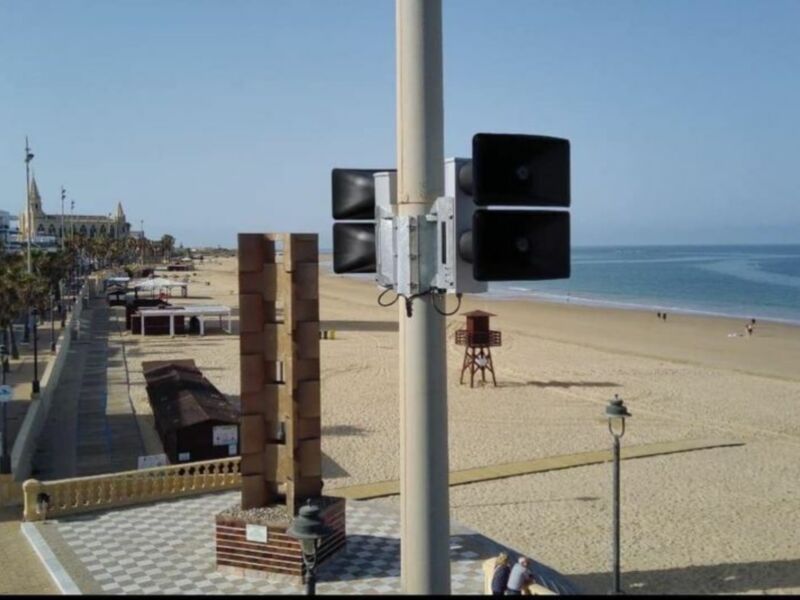 Playa con farola y señales de tráfico, edificios a la izquierda, cielo claro.