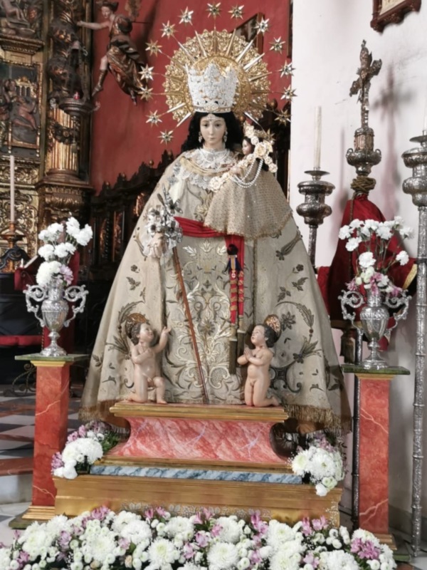 Imagen de una iglesia con un altar principal y flores blancas en el suelo.