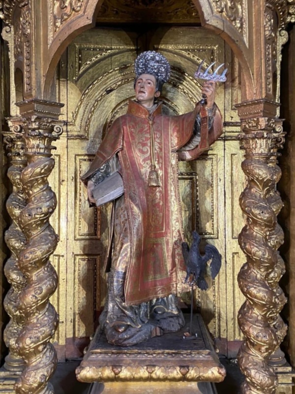 Elegante estatua religiosa con vestimenta ceremonial y corona, rodeada de detalles dorados en un entorno arquitectónico.