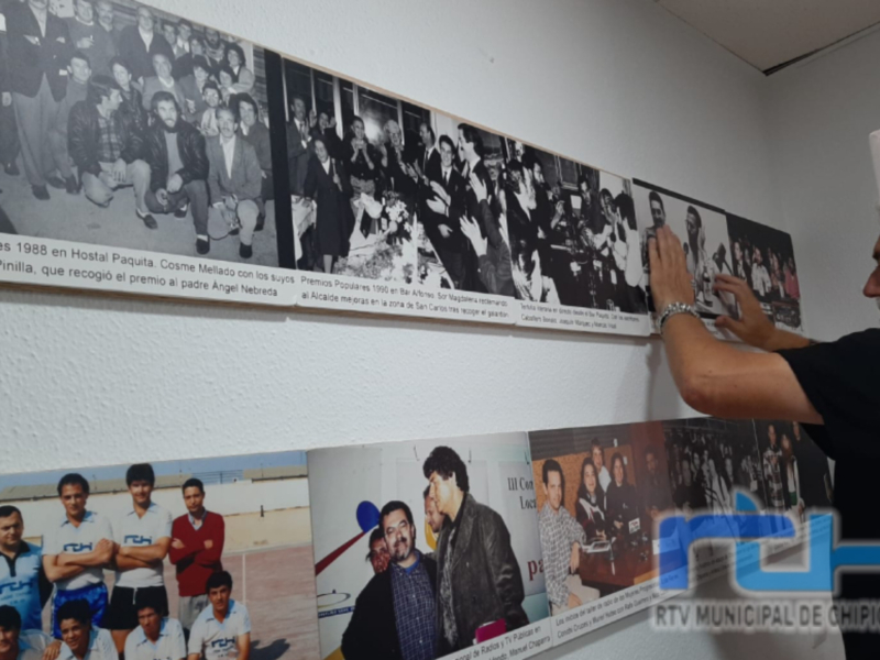 Un hombre toca una foto de un equipo de fútbol en la pared, con otros carteles históricos alrededor. La imagen es parte de una exposición en RTV Municipal de Chivilcoya.