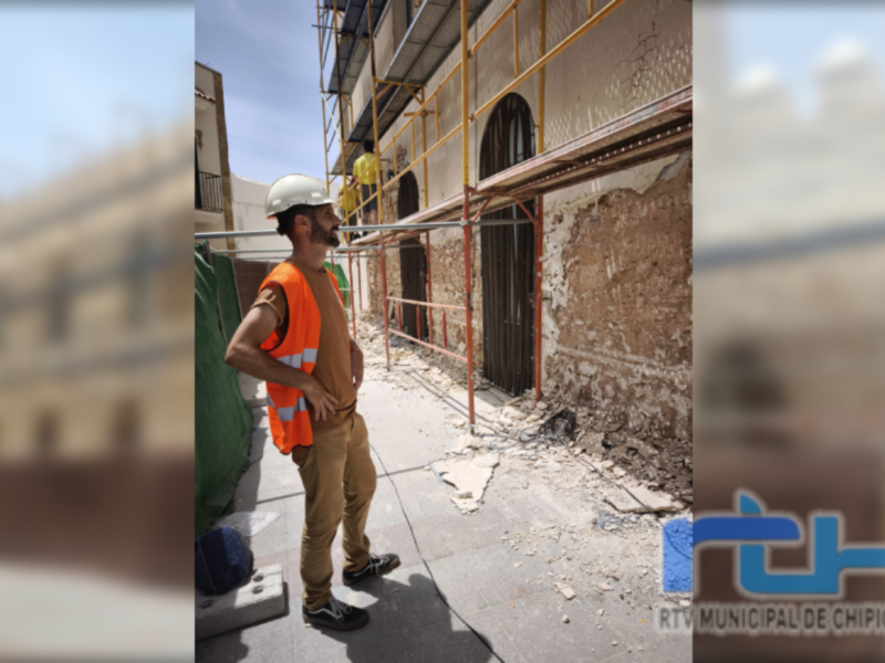 Un trabajador en un área de construcción, con una chaqueta naranja y casco blanco, frente a una pared desmoronada. La imagen es de Chipiona, provincia de Cádiz.