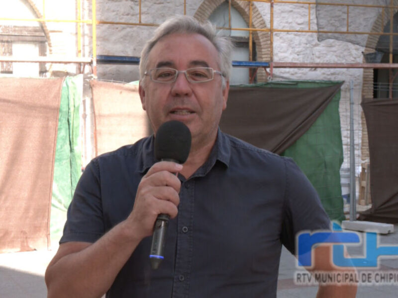 Un hombre habla en un micrófono mientras sostiene una bandera verde y marrón en el fondo.