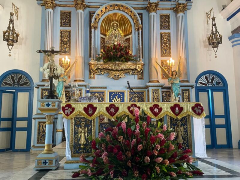 Altar de una iglesia con flores y estatuas, iluminado por dos lámparas.