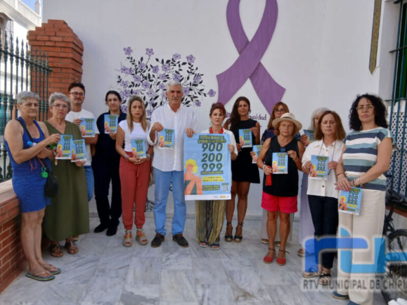 Una grupo de personas posa con carteles informativos en un evento de concientización sobre el cáncer de mama, con una corbata morada en el fondo.