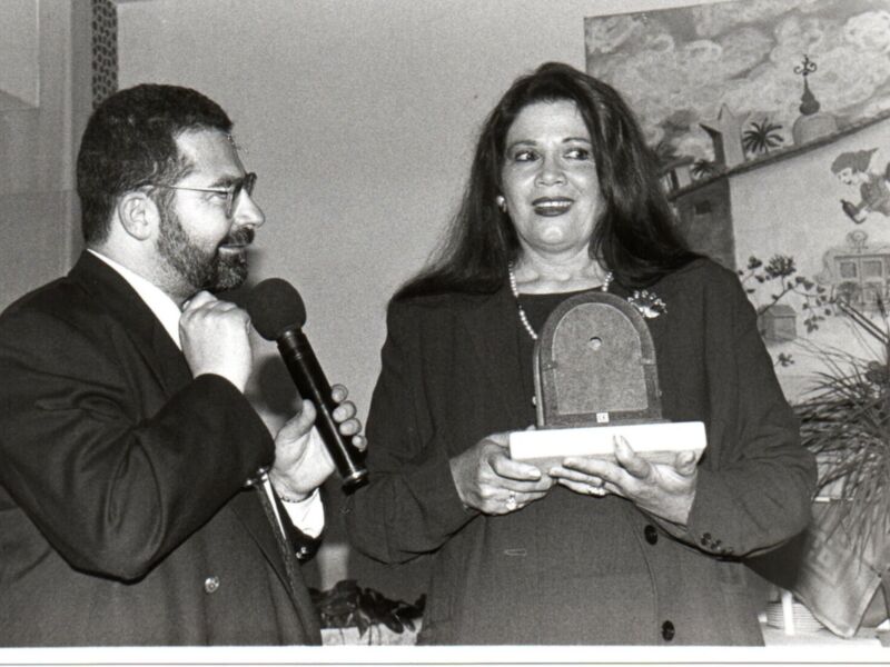 Una imagen en blanco y negro muestra a una mujer sonriendo mientras sostiene un regalo, con un hombre al lado que parece estar hablando por teléfono móvil.