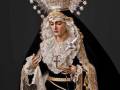 Una estatua de una Virgen María vestida con trajes elaborados y adornos dorados. Se observa un rostro sereno, una corona de estrellas y un manto negro con detalles florales dorados. La escena transmite una sensación de solemnidad y reverencia, típica en representaciones religiosas.